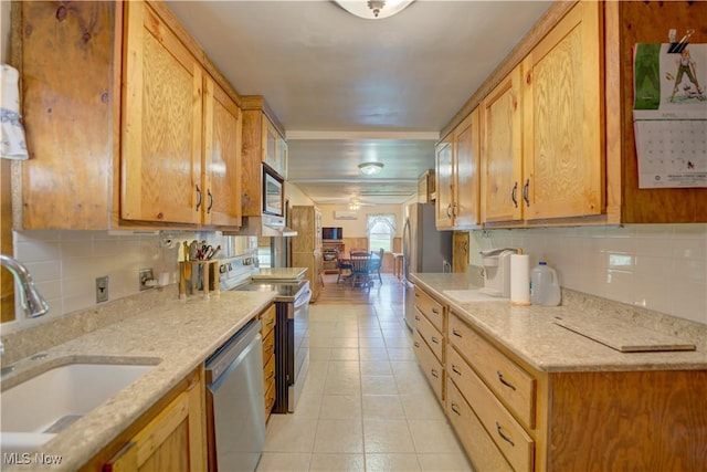 kitchen with appliances with stainless steel finishes, light stone counters, a sink, decorative backsplash, and light tile patterned floors