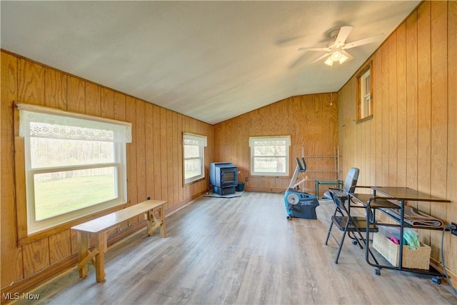 interior space with a ceiling fan, a wood stove, wood finished floors, lofted ceiling, and wooden walls