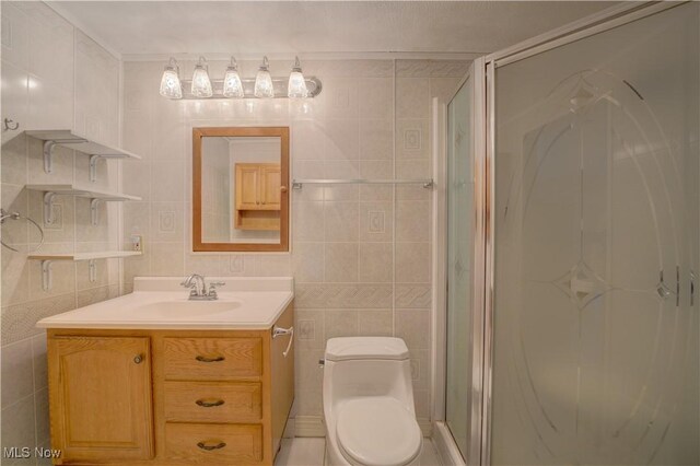 bathroom with toilet, tile walls, a shower stall, and vanity