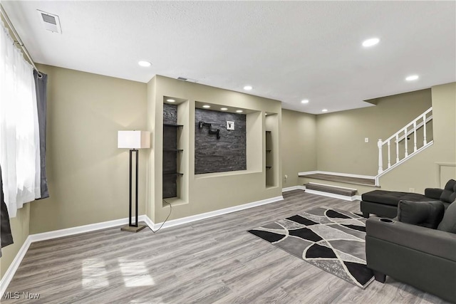living room featuring baseboards, visible vents, wood finished floors, and stairway
