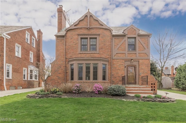 tudor home with brick siding and a front yard