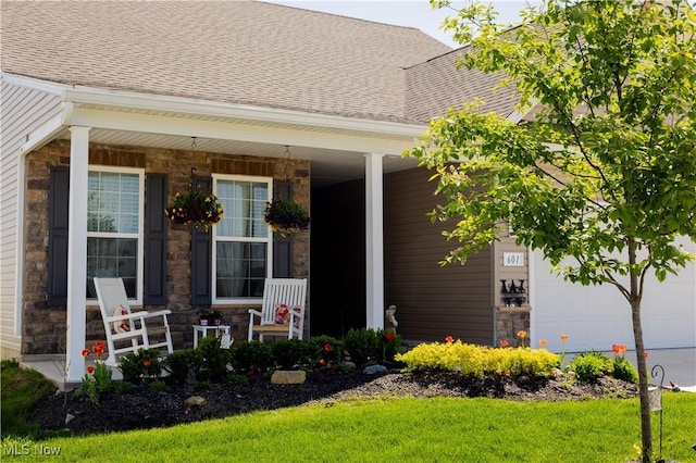 view of exterior entry with roof with shingles, covered porch, a garage, and stone siding