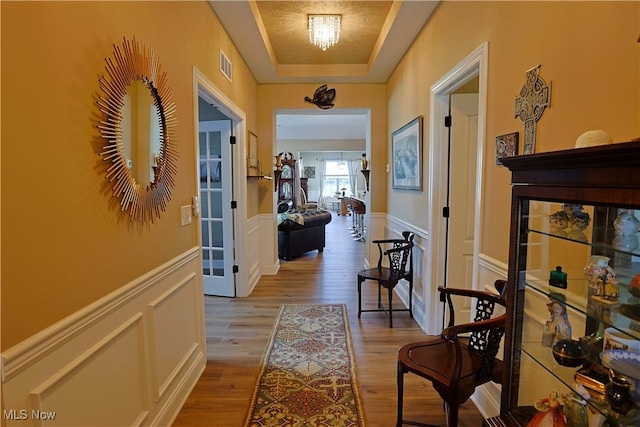 601 Cedar Crest Dr, Elyria, OH 44035 - corridor featuring light wood-style flooring, a decorative wall, a tray ceiling, and wainscoting