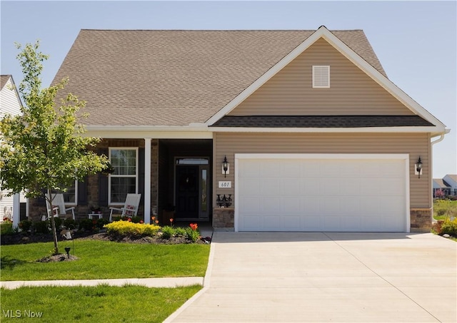 view of front of home with covered porch, driveway, a front yard, an attached garage, and stone siding