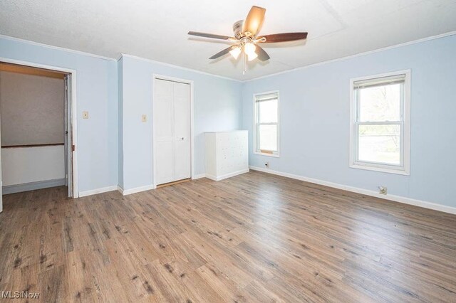 unfurnished bedroom with crown molding, a ceiling fan, baseboards, wood finished floors, and a closet