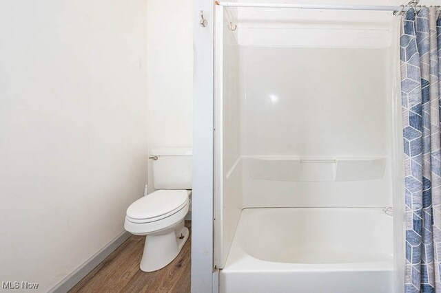 full bathroom featuring a shower with shower curtain, wood finished floors, toilet, and a washtub