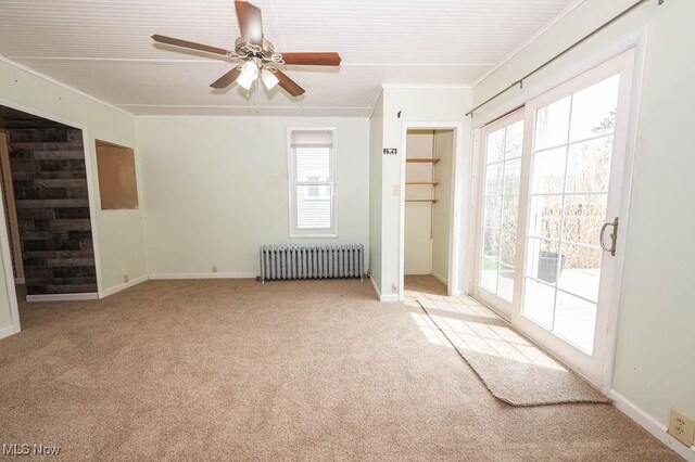 empty room with ceiling fan, crown molding, baseboards, radiator, and carpet flooring