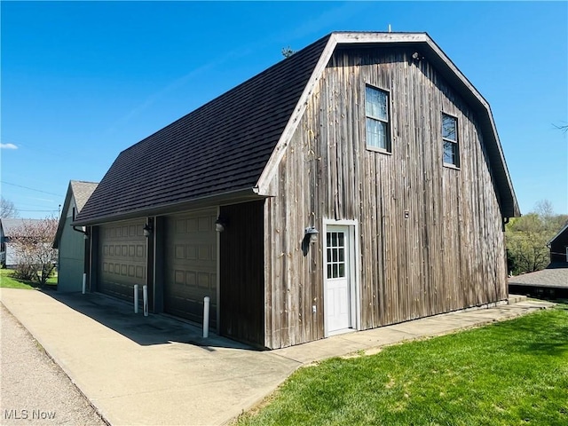 exterior space featuring a detached garage, an outdoor structure, roof with shingles, and a gambrel roof