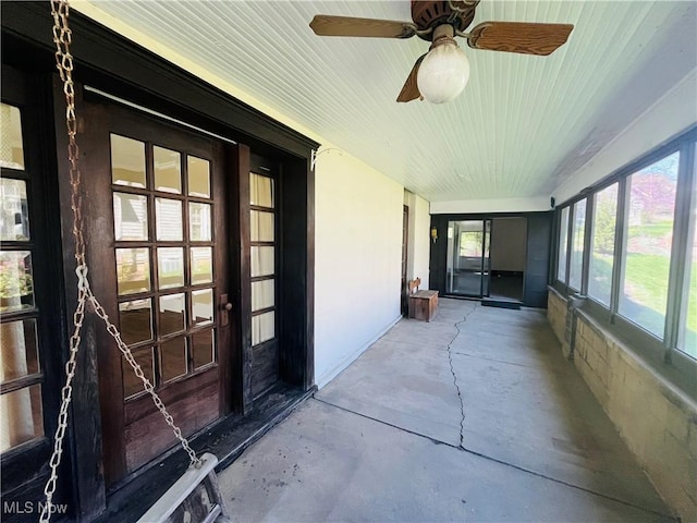 unfurnished sunroom featuring plenty of natural light, a ceiling fan, concrete floors, and wooden ceiling