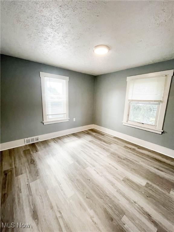 unfurnished room with plenty of natural light, a textured ceiling, and wood finished floors