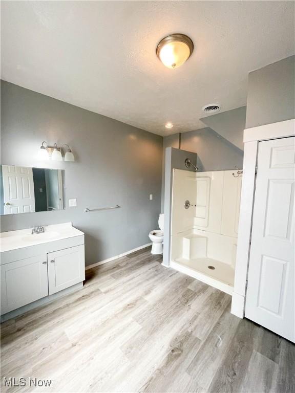 full bath with visible vents, vanity, wood finished floors, toilet, and a stall shower