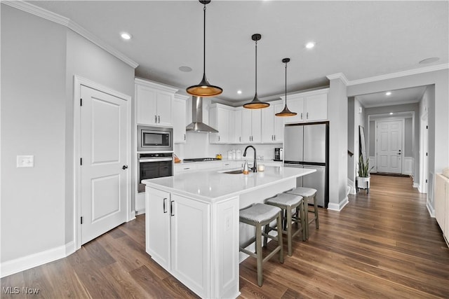 kitchen with crown molding, wall chimney exhaust hood, white cabinets, a sink, and appliances with stainless steel finishes