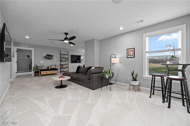 carpeted living room with a textured ceiling, baseboards, visible vents, and ceiling fan