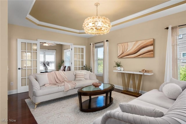 living room featuring a tray ceiling, an inviting chandelier, a healthy amount of sunlight, and wood finished floors