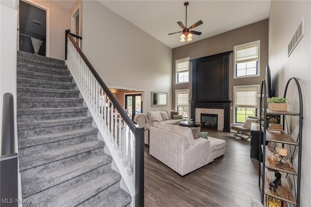 living room featuring a high ceiling, a ceiling fan, wood finished floors, visible vents, and stairway