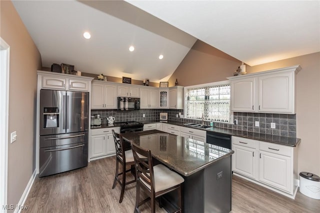 kitchen with a sink, a breakfast bar area, wood finished floors, vaulted ceiling, and black appliances