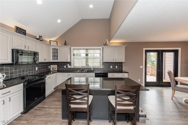 kitchen with dark countertops, a breakfast bar area, light wood-type flooring, a sink, and black appliances