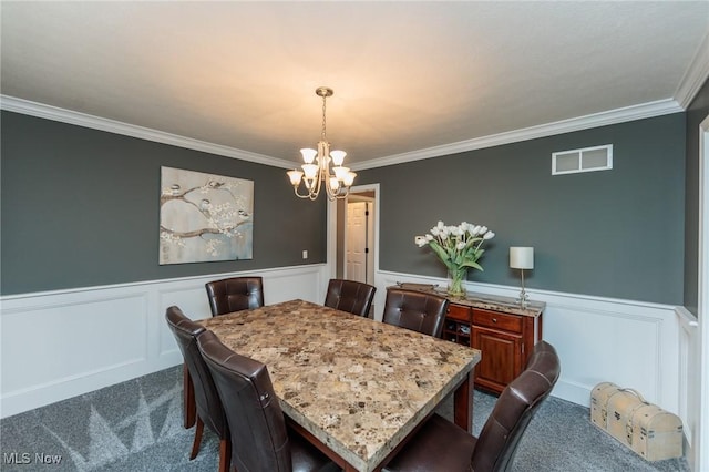 dining room featuring dark carpet, ornamental molding, a wainscoted wall, and an inviting chandelier
