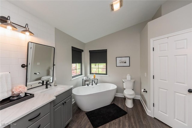 bathroom with vanity, toilet, a freestanding tub, wood finished floors, and lofted ceiling