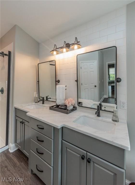 bathroom featuring wood finished floors, double vanity, a sink, and a stall shower