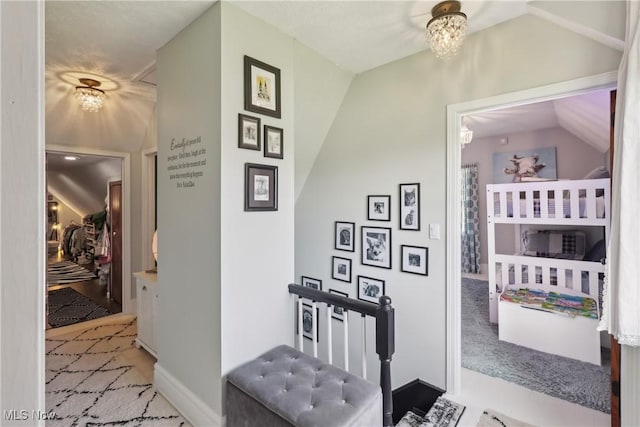 hall with baseboards, an upstairs landing, and lofted ceiling