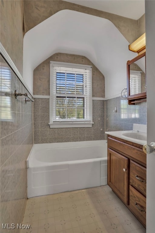 full bathroom with vanity, lofted ceiling, tile walls, tile patterned floors, and a tub to relax in
