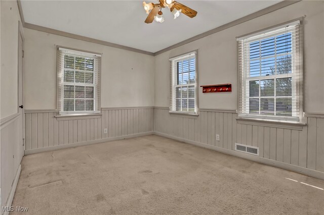 unfurnished room with a wainscoted wall, a ceiling fan, carpet flooring, and visible vents