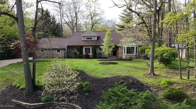 cape cod house with roof with shingles, a front lawn, and stone siding