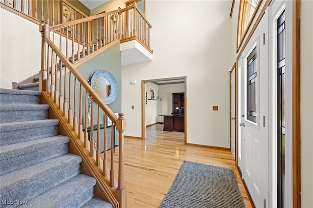 foyer entrance featuring stairway, baseboards, a high ceiling, and light wood-type flooring
