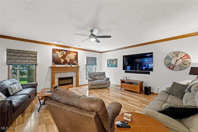 living area featuring a tiled fireplace, ornamental molding, light wood-style flooring, and ceiling fan