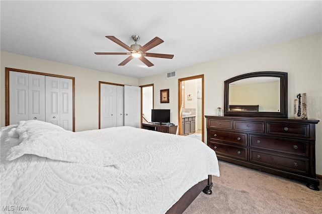 bedroom with ceiling fan, light carpet, multiple closets, ensuite bathroom, and visible vents
