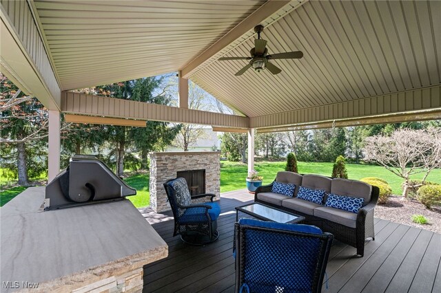 deck featuring a yard, a ceiling fan, and an outdoor living space with a fireplace