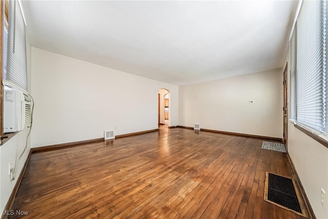 empty room featuring arched walkways, baseboards, hardwood / wood-style flooring, and visible vents