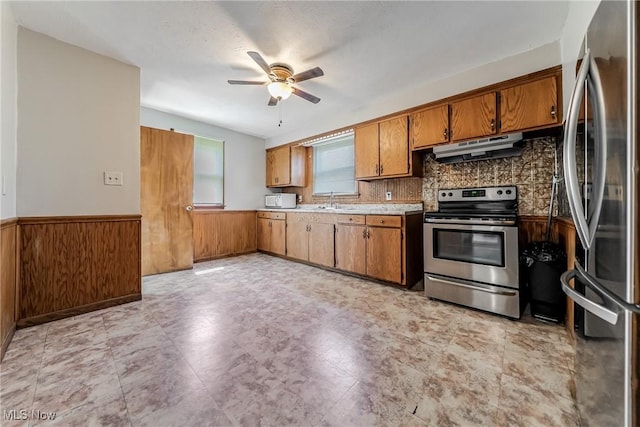 kitchen with a sink, appliances with stainless steel finishes, brown cabinetry, and under cabinet range hood