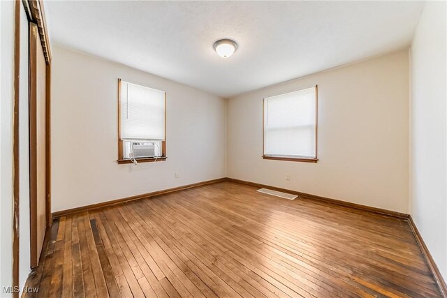 empty room featuring visible vents, baseboards, cooling unit, and hardwood / wood-style flooring
