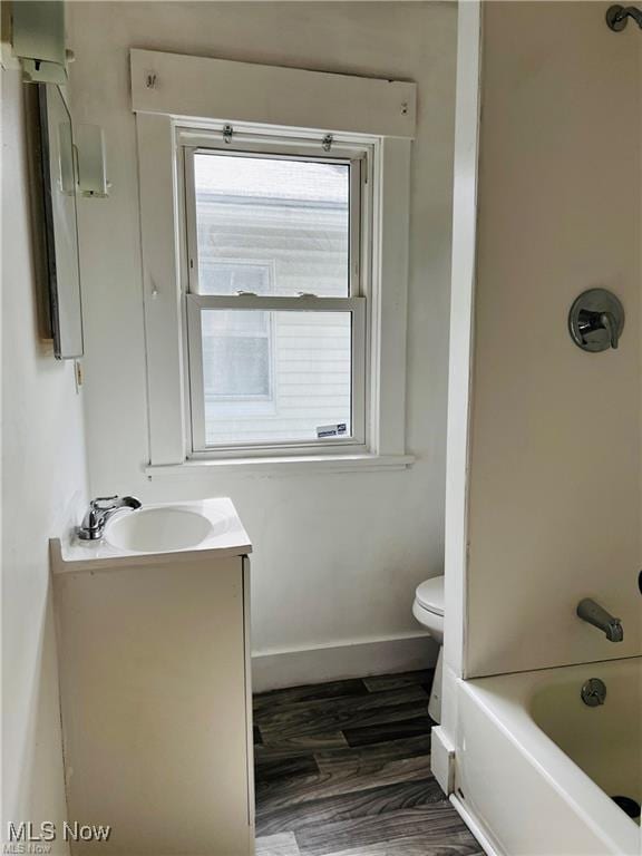 bathroom with wood finished floors, baseboards, vanity, toilet, and bathing tub / shower combination