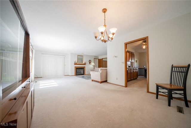 interior space with light colored carpet, a glass covered fireplace, ceiling fan with notable chandelier, baseboards, and visible vents