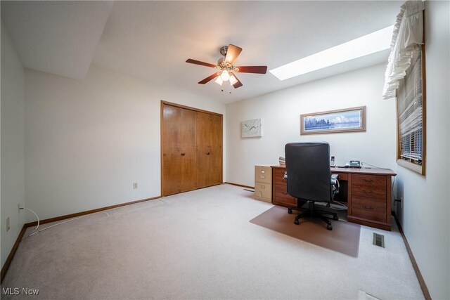 office featuring a skylight, baseboards, a ceiling fan, and light colored carpet