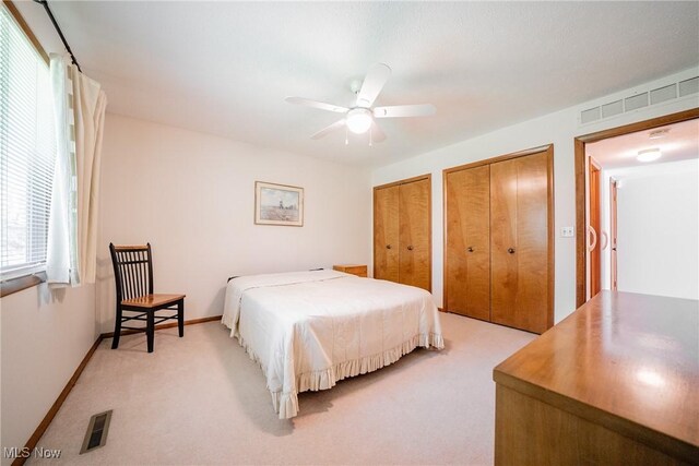 bedroom with multiple closets, visible vents, a ceiling fan, and light colored carpet