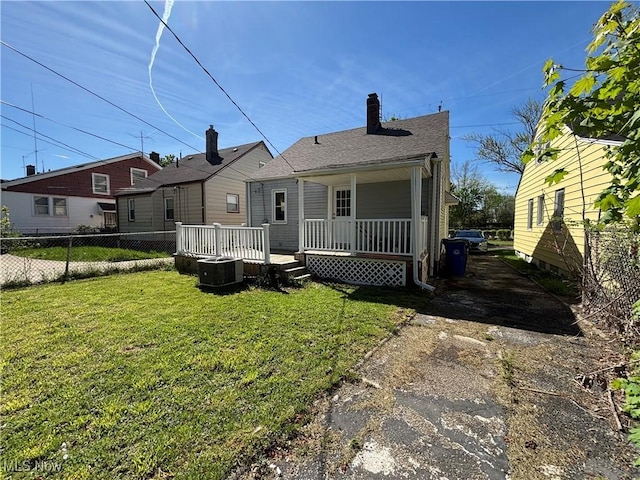 rear view of house featuring fence, cooling unit, a chimney, a porch, and a yard