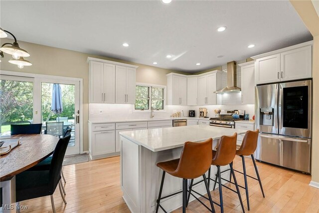 kitchen with wall chimney range hood, stainless steel appliances, decorative backsplash, and light wood-style flooring