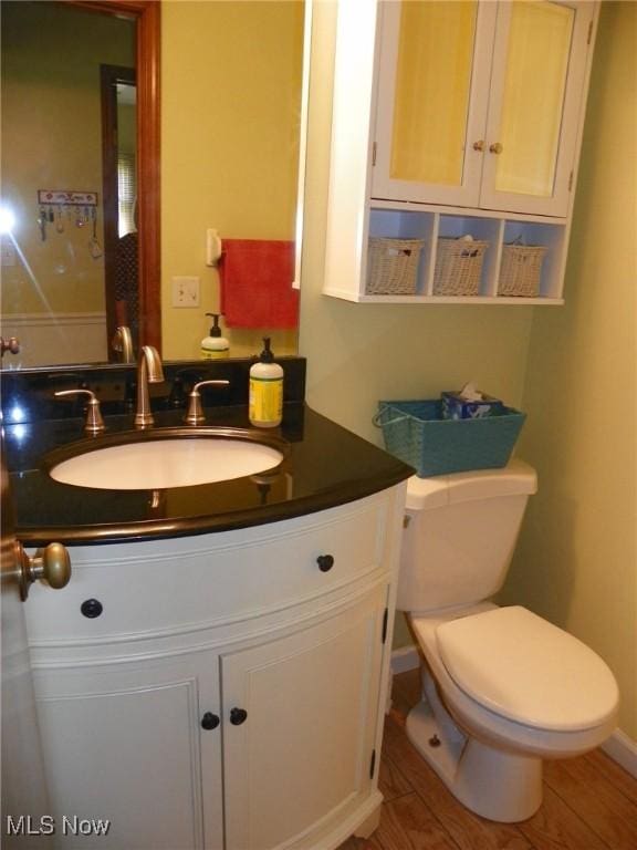 half bathroom featuring toilet, wood finished floors, and vanity