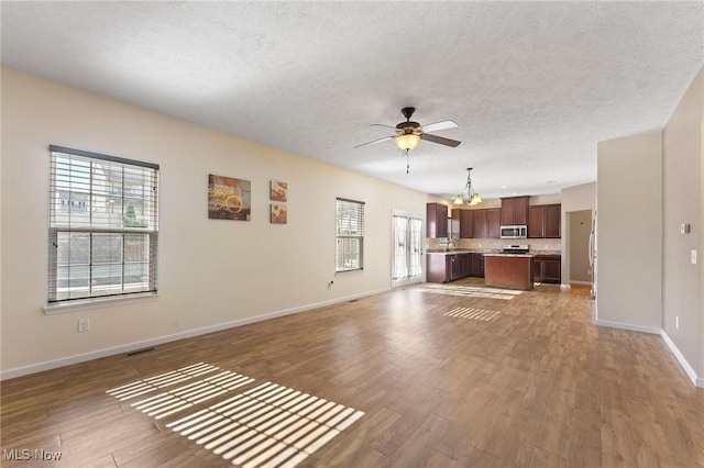 unfurnished living room with a textured ceiling, visible vents, wood finished floors, baseboards, and ceiling fan with notable chandelier