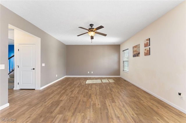 empty room featuring light wood-style floors, baseboards, stairway, and a ceiling fan
