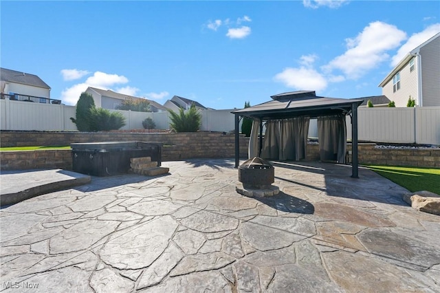 view of patio featuring a hot tub, a gazebo, a fire pit, and a fenced backyard