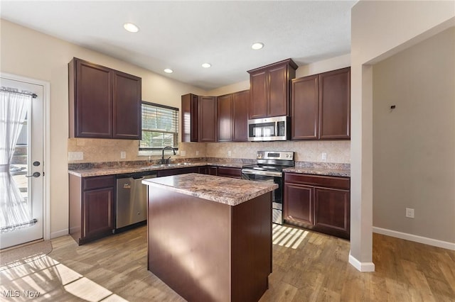 kitchen with a kitchen island, backsplash, appliances with stainless steel finishes, light wood-type flooring, and a sink
