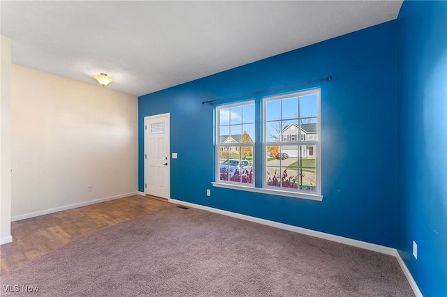 carpeted spare room with baseboards, wood finished floors, and visible vents