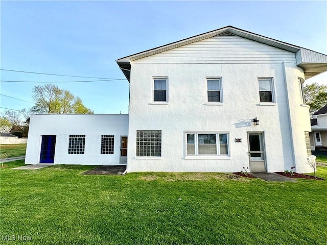 rear view of property featuring stucco siding and a yard