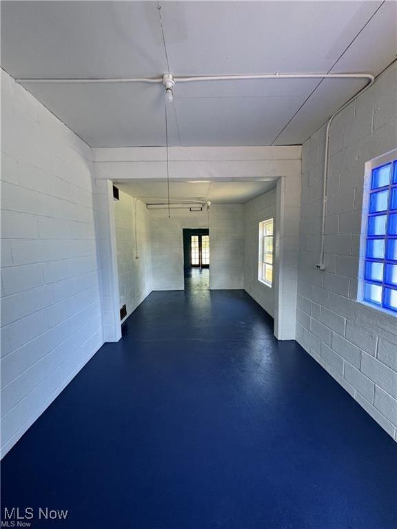 empty room with concrete block wall, concrete floors, and a healthy amount of sunlight