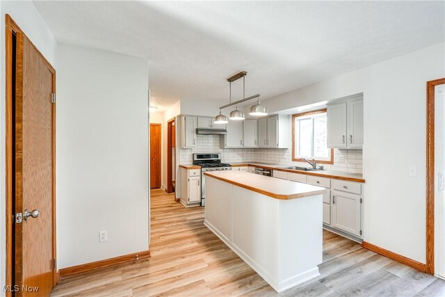 kitchen featuring backsplash, under cabinet range hood, light wood-style flooring, and gas range